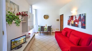 A modern living room with a red sofa, a flat-screen TV, a dining area with a table and chairs, and artwork on the walls. - Casa Lido beautiful lake view (Varenna)