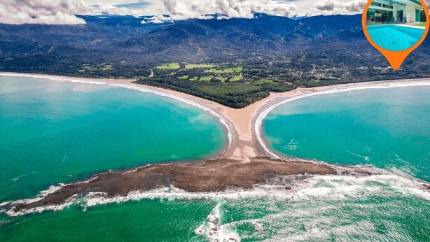 Vista aérea de una zona costera con una playa extensa y montañas al fondo.