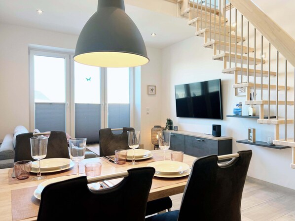 Uma sala de jantar moderna com uma mesa de madeira posta para quatro pessoas, uma luminária pendente grande e uma escada com corrimão de madeira.