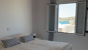 A bedroom with a large bed, a window with a view of the sea, and a ceiling fan. - Ferienwohnung (ΜΥΚΟΝΟΣ)
