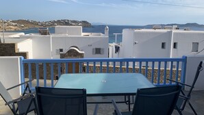 A balcony with a table and chairs overlooking a coastal town with white buildings and a view of the sea. - Ferienwohnung (ΜΥΚΟΝΟΣ)