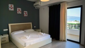 A hotel room with a large bed, a nightstand, a wall-mounted air conditioner, and a view of the sea through a balcony. - Privé City Hotel (Sarandë)