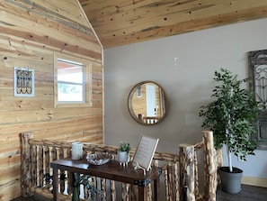 L'intérieur d'un chalet rustique, avec un mur en bois, un miroir rond, une table agrémentée d'objets décoratifs et une plante en pot.