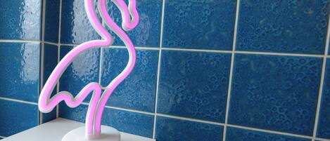 Een neon vlamingo bord op een witte basis tegen een blauwe betegelde muur.