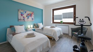 Un dormitorio con dos camas, una ventana con persianas, una silla y una cinta de correr.