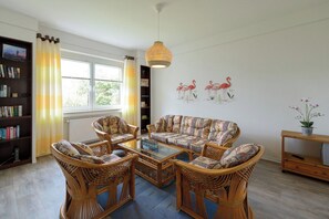 Un salon comprenant un canapé, des fauteuils, une table basse, une bibliothèque et un mur décoré d’œuvres d’art représentant des flamants roses.