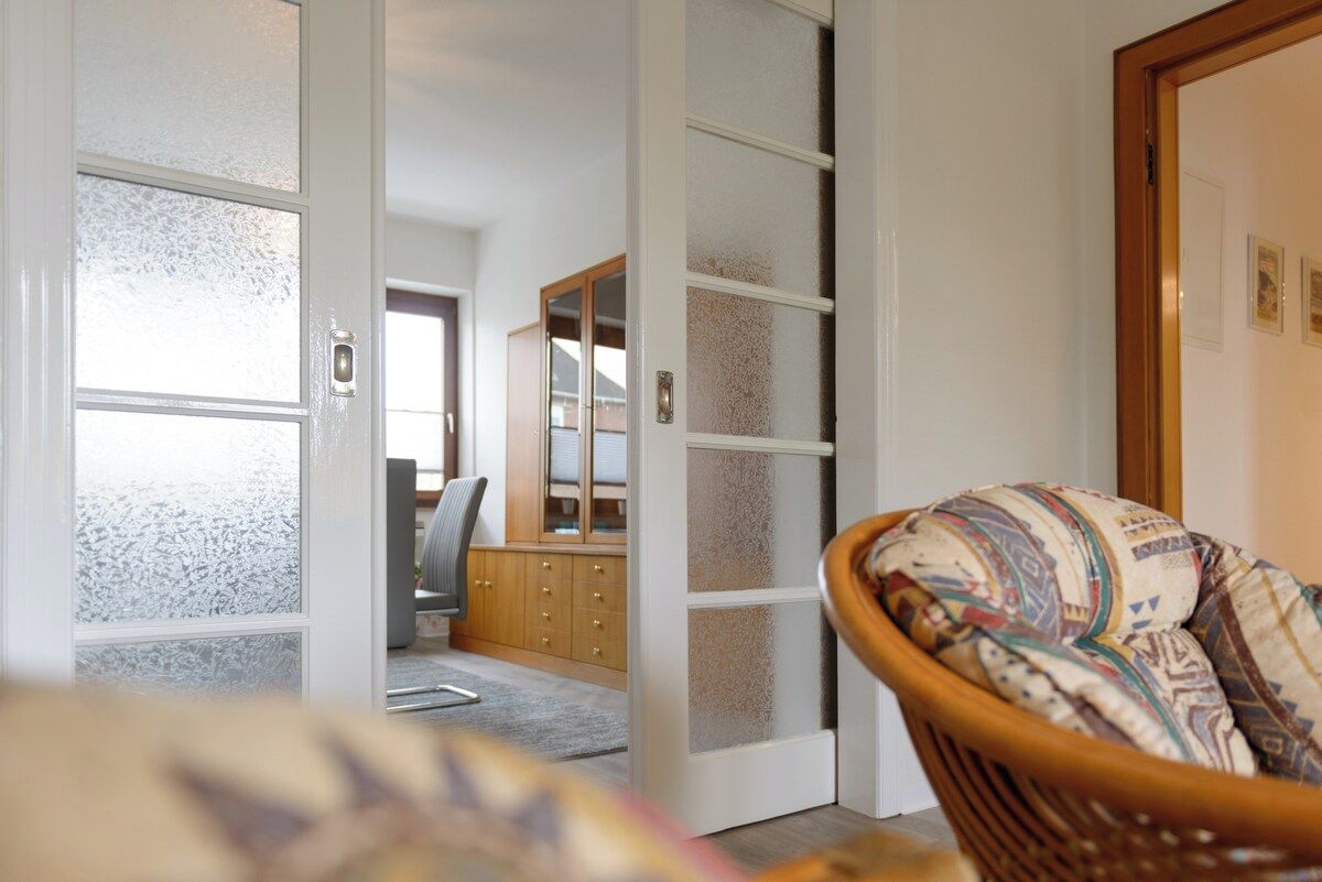Ein Zimmer mit Holztür, Korbsessel und einer Kommode mit Schubladen.
