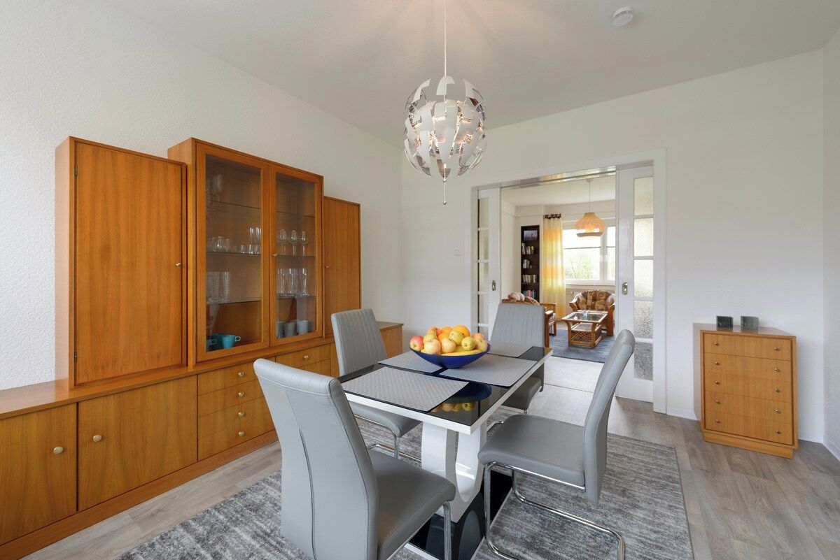 Un coin repas comprenant un buffet en bois, un lustre et une table avec des chaises.