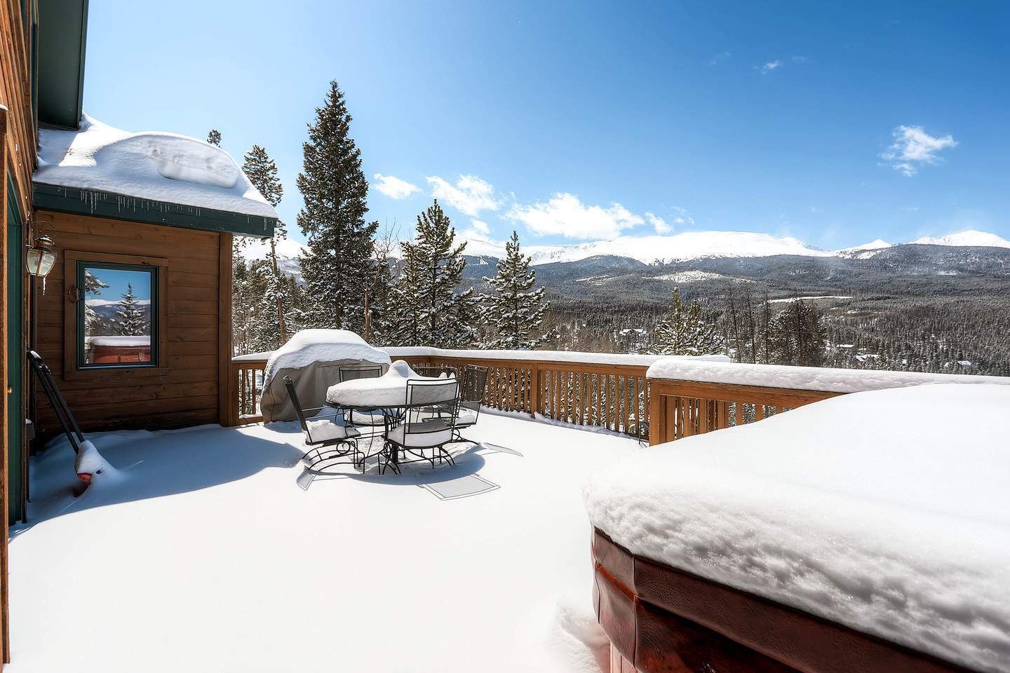 Een sneeuwtapijt op het terras met een tafel, stoelen, een barbecue en een uitzicht op besneeuwde bergen.