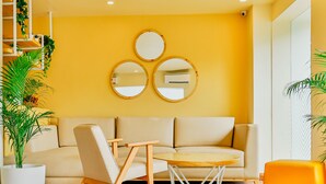 A modern living room with a sofa, a coffee table, and a chair. There are three wall-mounted mirrors and a potted plant. - Bloom Hotel - Worli (Mumbai)
