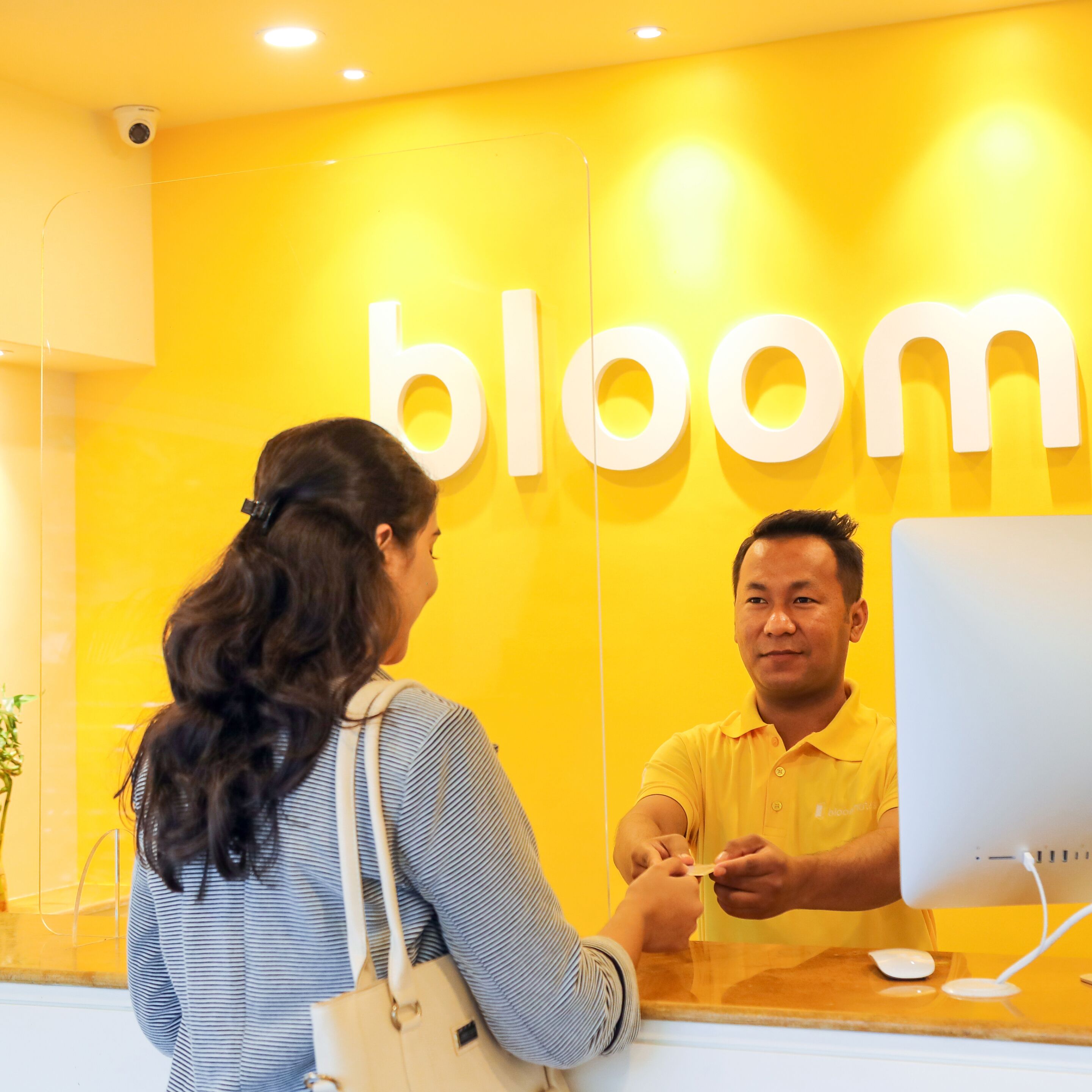 Un mostrador de recepción con un letrero que dice 'bloom', un monitor de computadora y una persona interactuando allí.