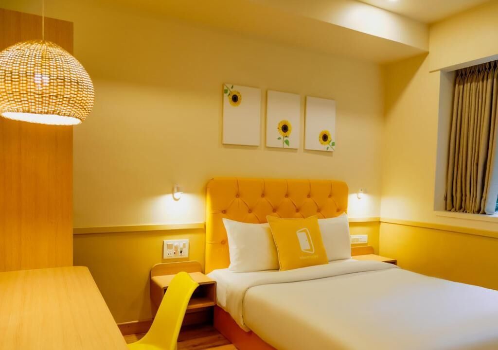 Une chambre d’hôtel avec un lit, un luminaire suspendu, une fenêtre avec des rideaux et trois tableaux accrochés au mur.