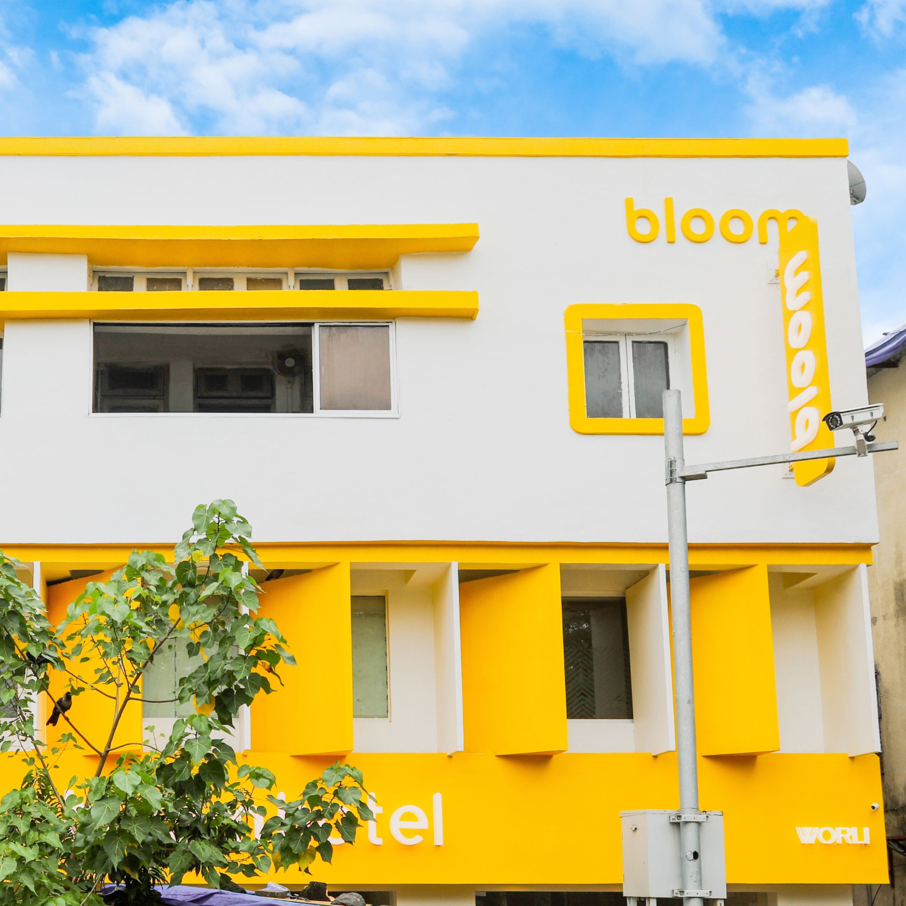 A hotel with a yellow and white facade, multiple windows, and a visible security camera.