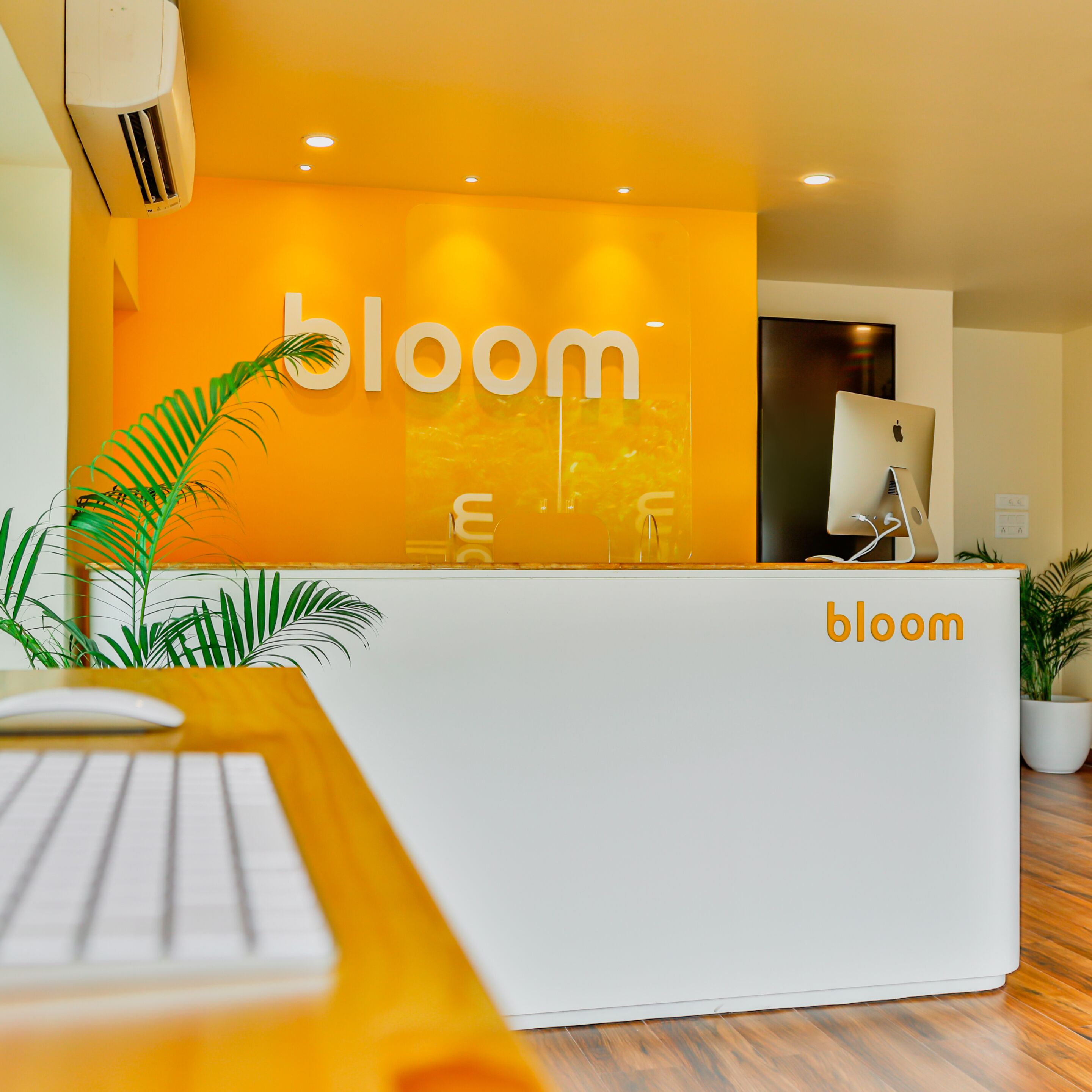 Ein Empfangsschalter mit einem Schild mit der Aufschrift 'bloom', einem Computer und einer Tastatur auf einem Holztisch.