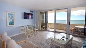 Un soggiorno con un tavolino in vetro, sedie, un divano e una televisione. È presente un balcone con vista sull'oceano.