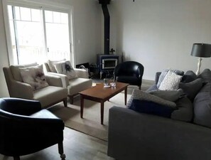 Relax in a spacious living room with a central seating area, featuring a beige sofa, a black armchair, and a grey sofa with decorative pillows.