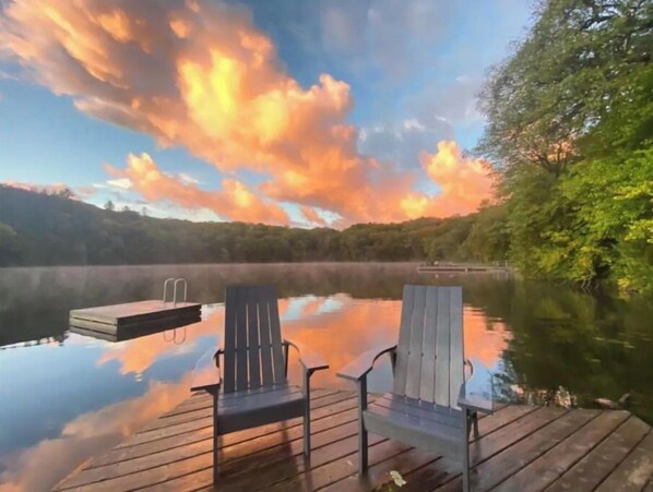Relax in Adirondack chairs on a serene lakeside dock surrounded by lush greenery.