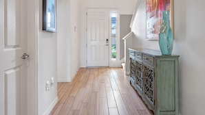 A hallway with wooden flooring, white walls, a white door, a green cabinet, and a colorful painting. - Arcade, Caribbean Pool Area, Foosball, Waterpark, 15 mins to Disney: The Springs (Davenport)
