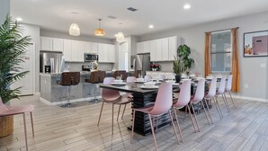A modern kitchen with white cabinets, stainless steel appliances, and a central island with pink chairs. - Arcade, Caribbean Pool Area, Foosball, Waterpark, 15 mins to Disney: The Springs (Davenport)