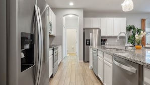 A modern kitchen with stainless steel appliances, white cabinetry, and a granite countertop. - Arcade, Caribbean Pool Area, Foosball, Waterpark, 15 mins to Disney: The Springs (Davenport)