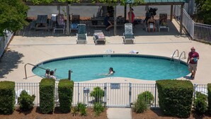 Ein Swimmingpool mit Liegestühlen, einer überdachten Sitzgelegenheit und einem umzäunten Poolbereich.
