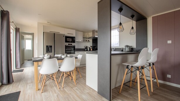 A modern kitchen with white cabinets, a dining area with white chairs, and a bar area with stools.