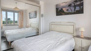 A bedroom with two beds, a painting on the wall, and a window with curtains. - 50m from the beach, seaview flat for 5 (Pornichet)