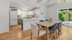 Een moderne keuken met witte kasten, een centraal eiland en een eethoek met een houten tafel en stoelen.
