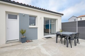 A modern house with a patio, a sliding glass door, and a small table with chairs. - House with garden, sleeps 6 adults, 1 child (Saint-Michel-Chef-Chef)