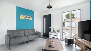 Un soggiorno moderno con un divano grigio, un tavolino in legno, una televisione e una porta scorrevole in vetro che dà su una zona esterna.