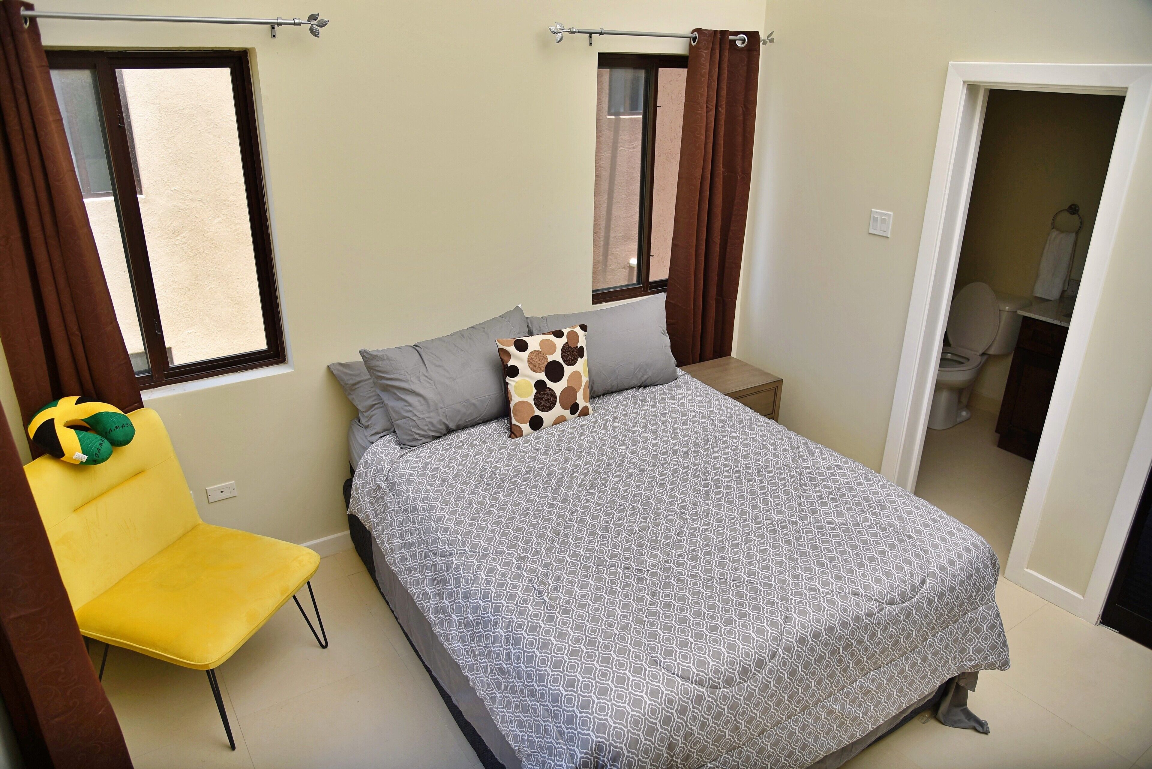 A bedroom with a bed, a chair, a window, and a door leading to a bathroom.
