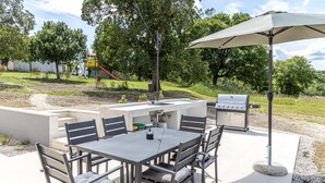 An outdoor patio with a table and chairs, a grill, and a play structure in the background. - Beautiful Villa Gallova (Labin)