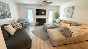 A living room with a fireplace, a ceiling fan, and a large TV.