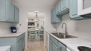 A narrow kitchen with light blue cabinets, a white countertop, and a stainless steel sink.
