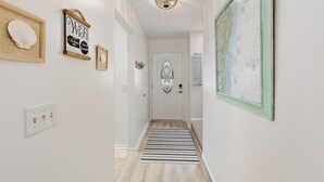 A hallway with a wooden floor, a striped rug, and a door with a decorative glass panel.