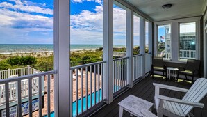Eine überdachte Veranda mit Blick auf den Strand, einen Pool und Sitzgelegenheiten im Freien.