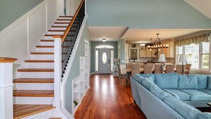 Ein geräumiger Wohnbereich mit einer Holztreppe, einem hellblauen Sofa und einer Küche im Hintergrund.