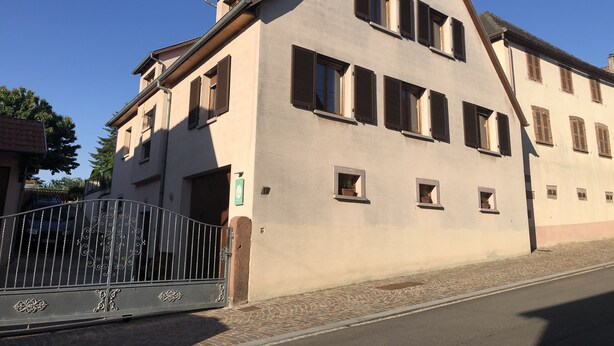 Un edificio de dos pisos con techo inclinado y varias ventanas con persianas.