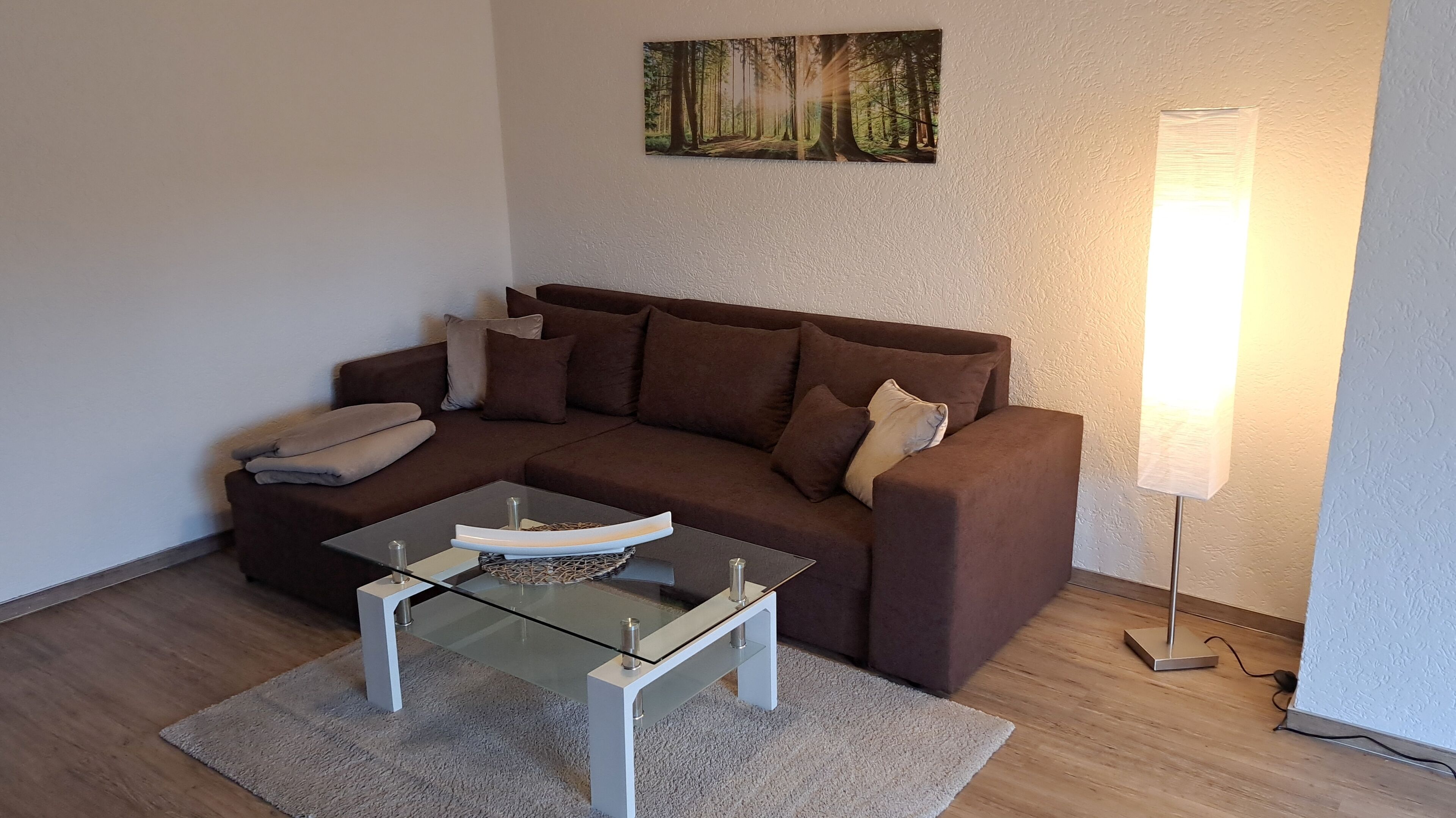 Ein Wohnzimmer mit braunem Sofa, einem Glastisch und einem Bild an der Wand.