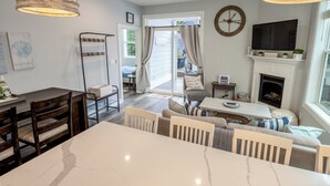 A modern living room with a fireplace, a dining area with a marble table, and a large window with curtains. - Beachwalk Resort Cottage with Pool Access/Golf Cart (Michigan City)
