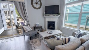 A living room with a fireplace, a television, and a view of the outside. - Beachwalk Resort Cottage with Pool Access/Golf Cart (Michigan City)