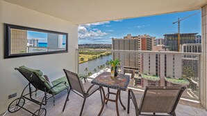 A balcony with a view of a river, a table with a plant, and two chairs. - Golf Course & Mountain Views at the Island Colony Amazing Building Amenities (Honolulu)