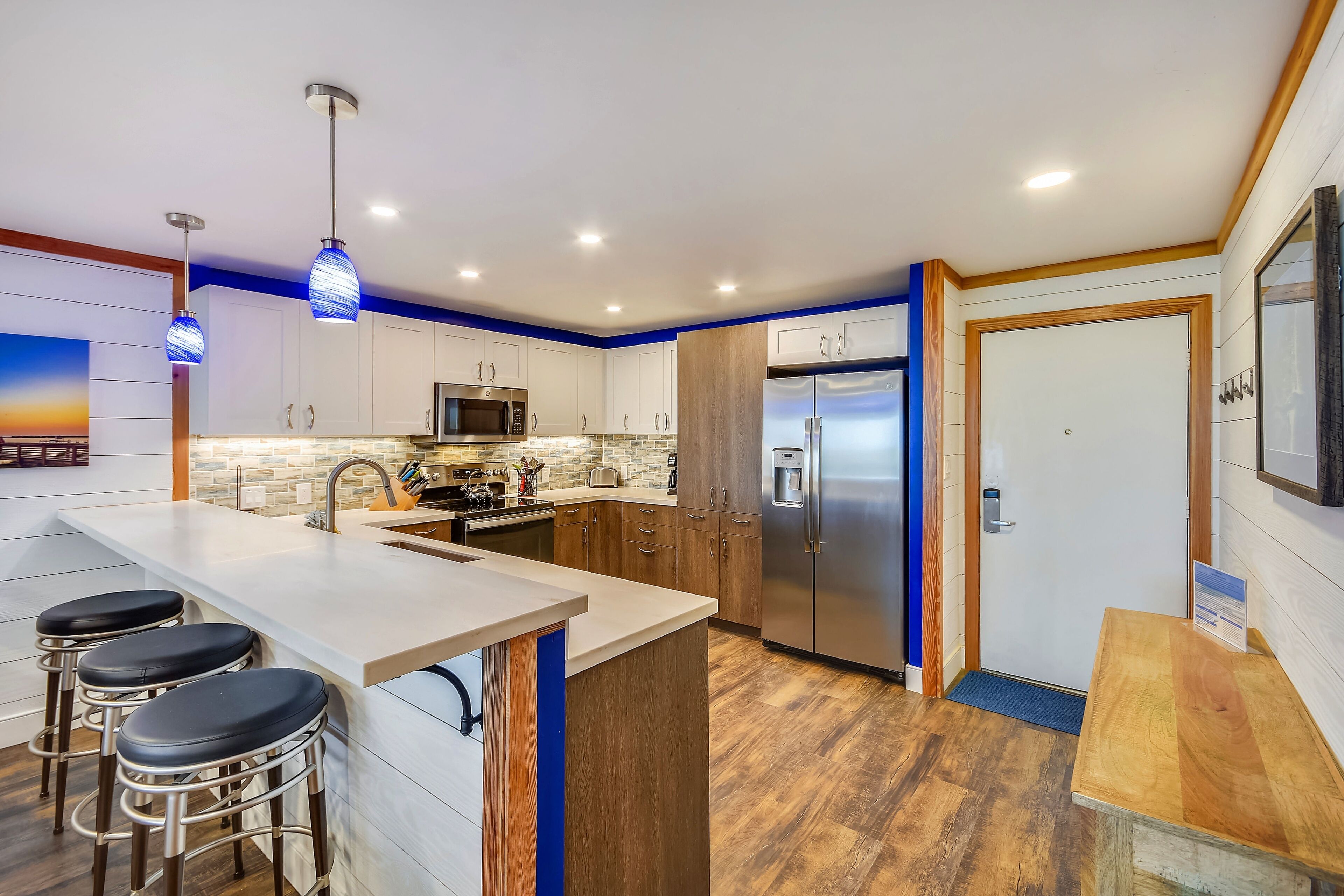 A modern kitchen with white cabinets, a stainless steel refrigerator, and a bar area with stools.