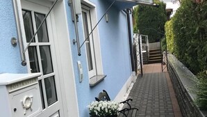 Ein schmaler Pfad führt zu einem blauen Gebäude mit weiß gefassten Fenstern und einer Glasmarkise.