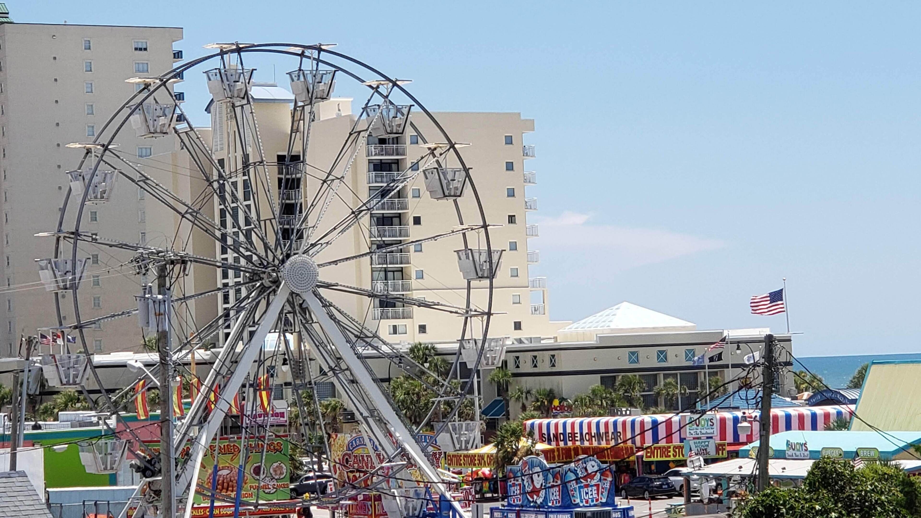 Une grande roue, un immeuble à plusieurs étages et un parc d’attractions en bord de mer, avec différents stands de nourriture.