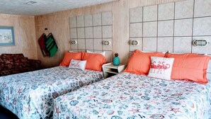 A hotel room with two beds, each with a floral-patterned bedspread, a wooden headboard, and a small nightstand with a lamp.