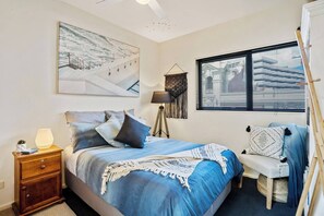 Un dormitorio con cama, mesita de noche, lámpara y un ventanal con persianas.