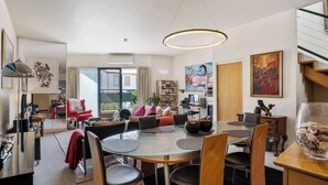 A modern living room with a glass dining table, comfortable seating, and artwork on the walls.
