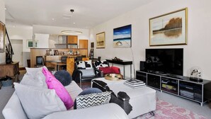 A modern living room with a sofa, a coffee table, a TV, and a kitchen in the background.