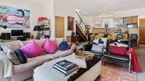 A modern living room with a sofa, coffee table, and a bookshelf. There is a staircase leading to an upper floor.